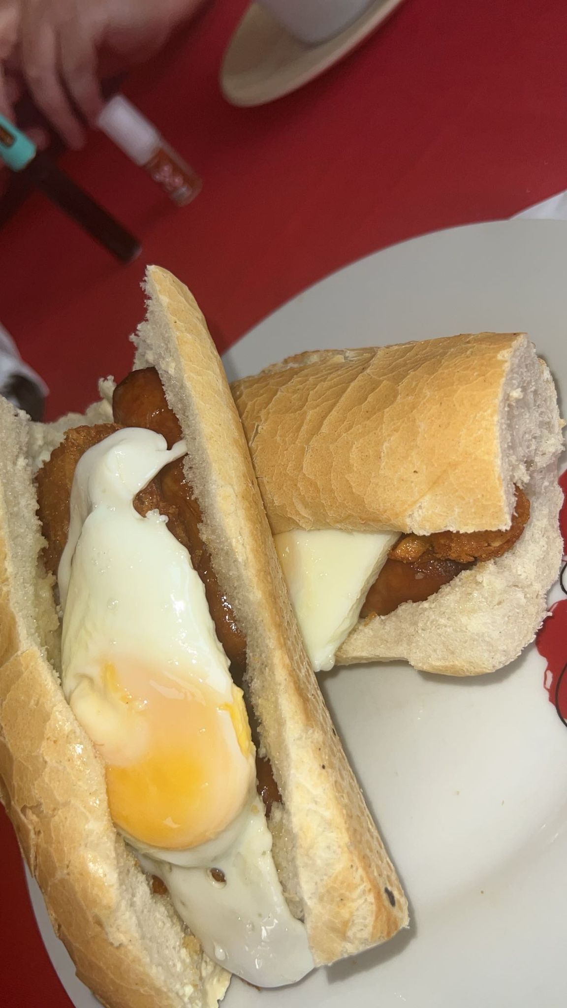 Un sándwich con un huevo frito y queso fundido sobre un plato blanco.