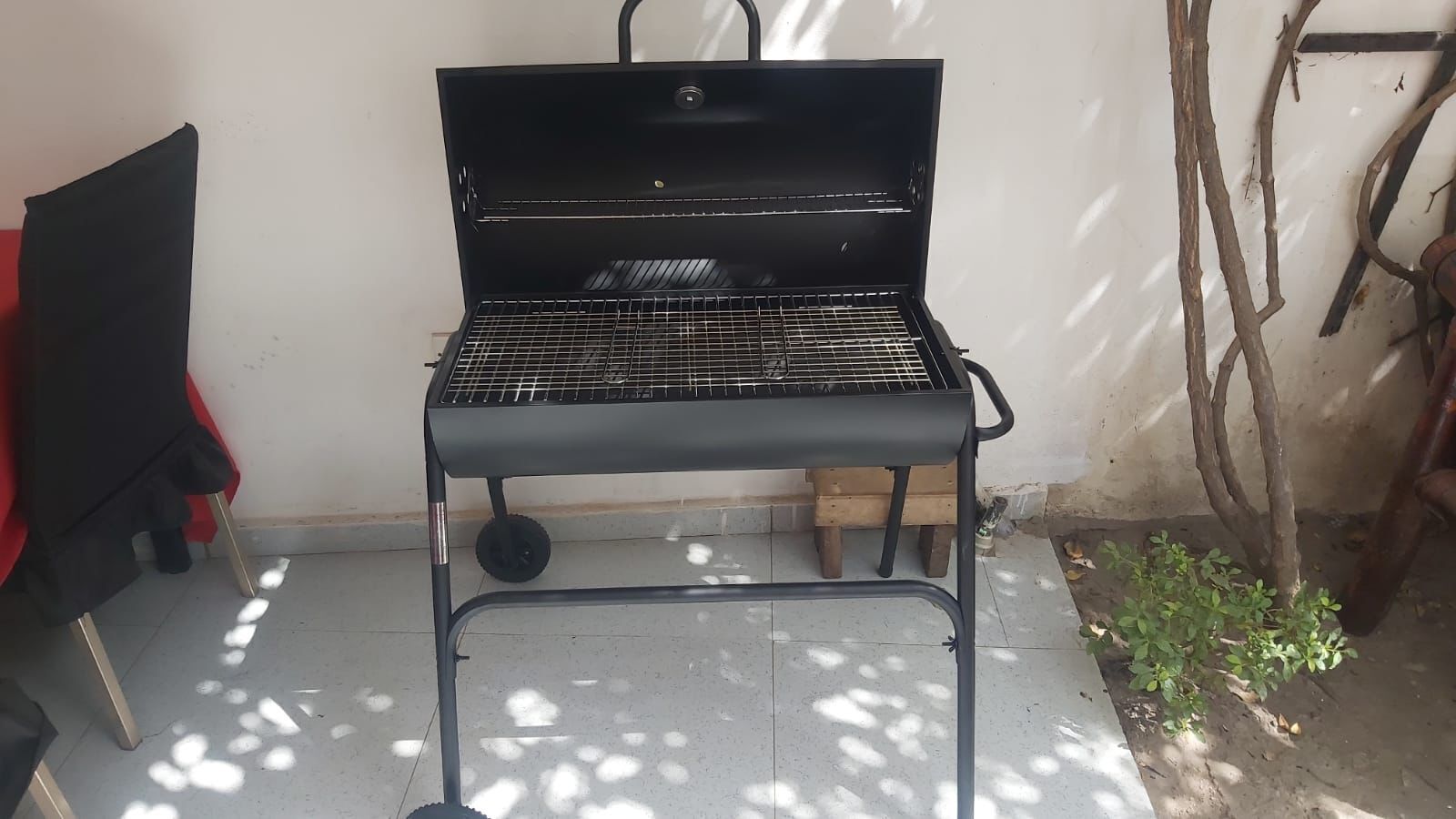 A black grill with a metal frame, positioned on a tiled floor with shadows cast by nearby objects.