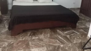 Un dormitorio con cama, paredes blancas, una ventana pequeña y una puerta.