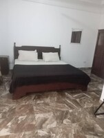 Un dormitorio con cama, paredes blancas, una ventana pequeña y una puerta.