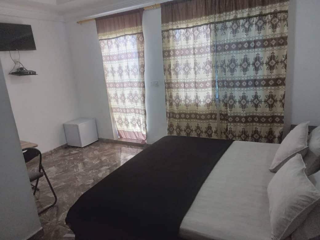 Un dormitorio con cama, cortinas, televisor y altavoz.