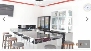 Una cocina moderna con una isla central, taburetes de bar, un refrigerador y un reloj en la pared.