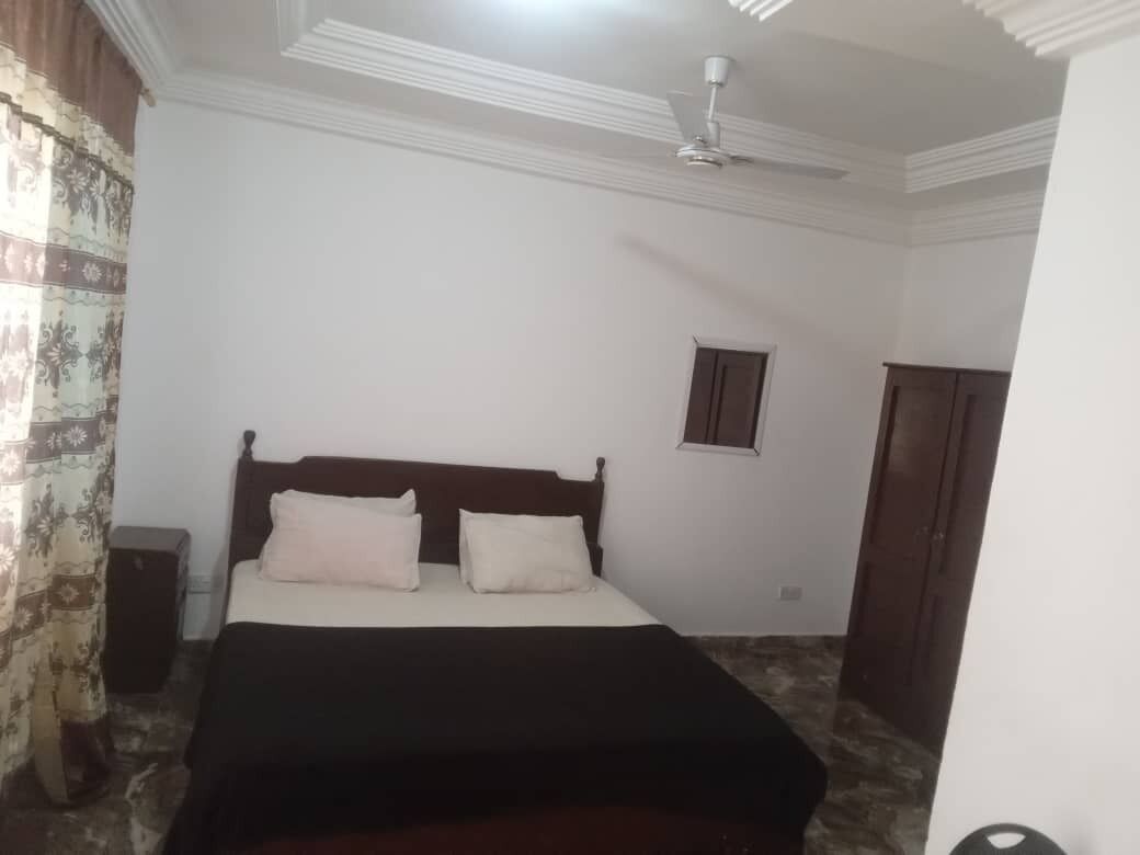 A bedroom with a bed, a ceiling fan, a small window, and a door.