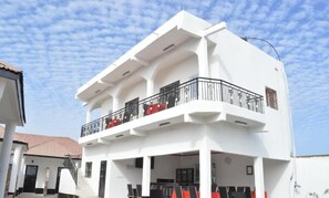 Un edificio de dos pisos con balcón, zona de estar al aire libre y una escalera que lleva a la entrada.