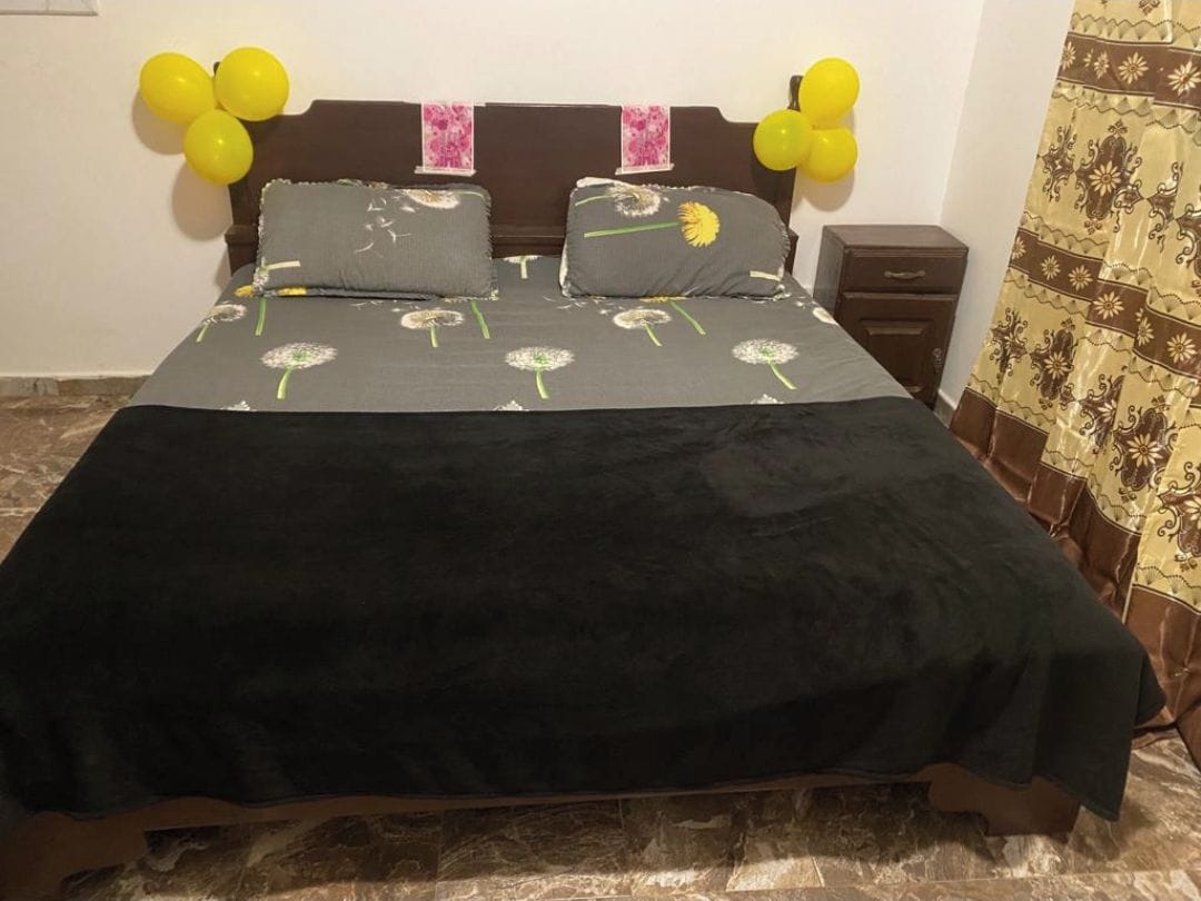 Un letto con copriletto nero e cuscini, una testiera in legno e palloncini gialli appesi al muro.