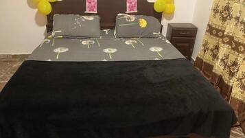 Un letto con copriletto nero e cuscini, una testiera in legno e palloncini gialli appesi al muro.