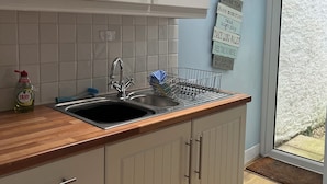 A kitchen with white cabinets, a wooden countertop, a sink, and a window with a view of the outside.