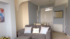 A living room with a grey sectional sofa, a small ottoman, and a dining area in the background.