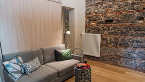 A modern living room with a grey sofa, patterned cushions, a small round table with a book and glass, and a stone wall. - Beachfront apartment in San Giovanni li Cuti suitable for families (Catania)