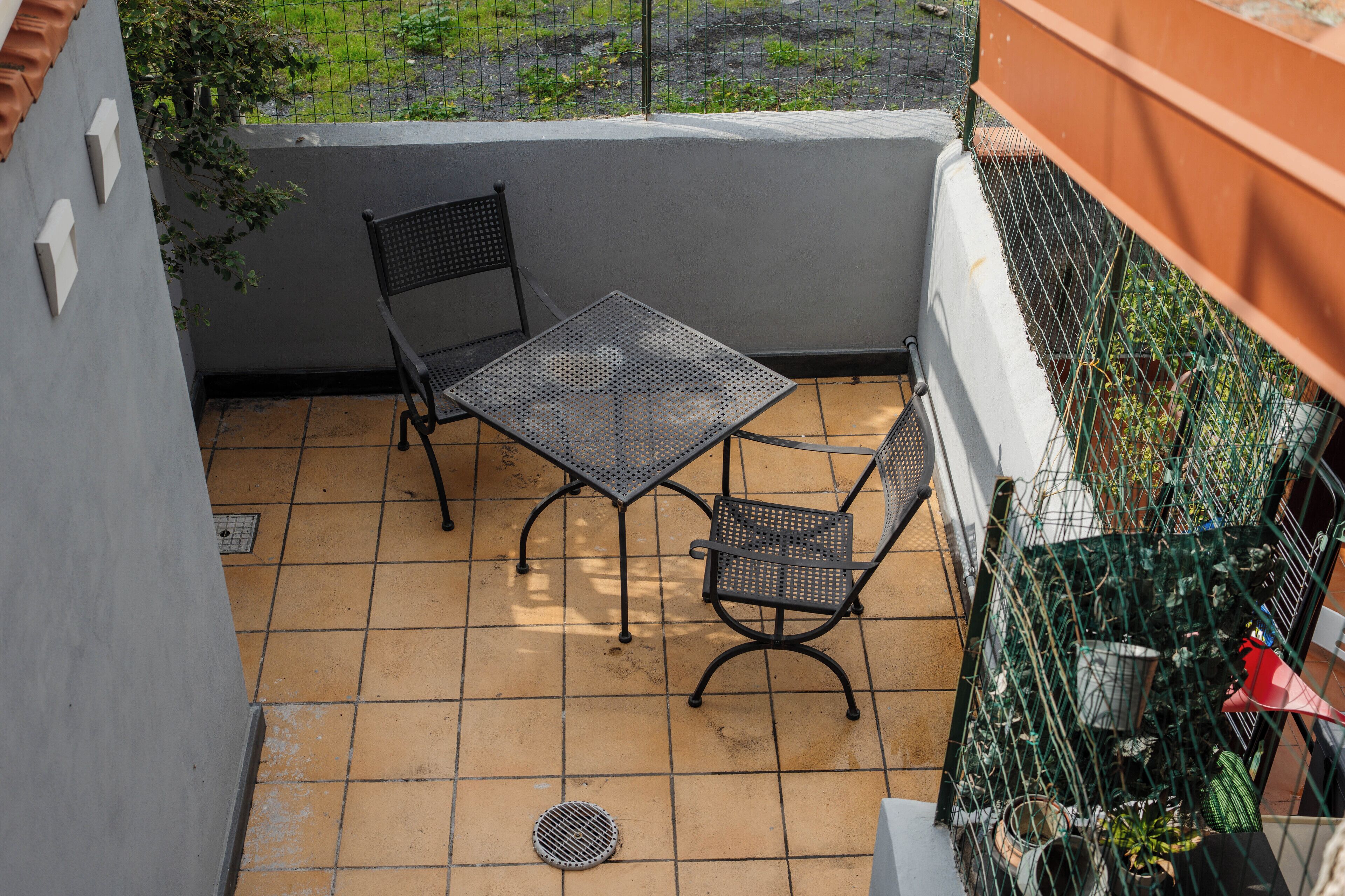 A balcony with two metal chairs and a table, surrounded by a metal fence and potted plants.