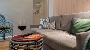 A living room with a grey sofa, a wicker side table with a book and a glass of red wine, and a teal chair. - Beachfront apartment in San Giovanni li Cuti suitable for families (Catania)