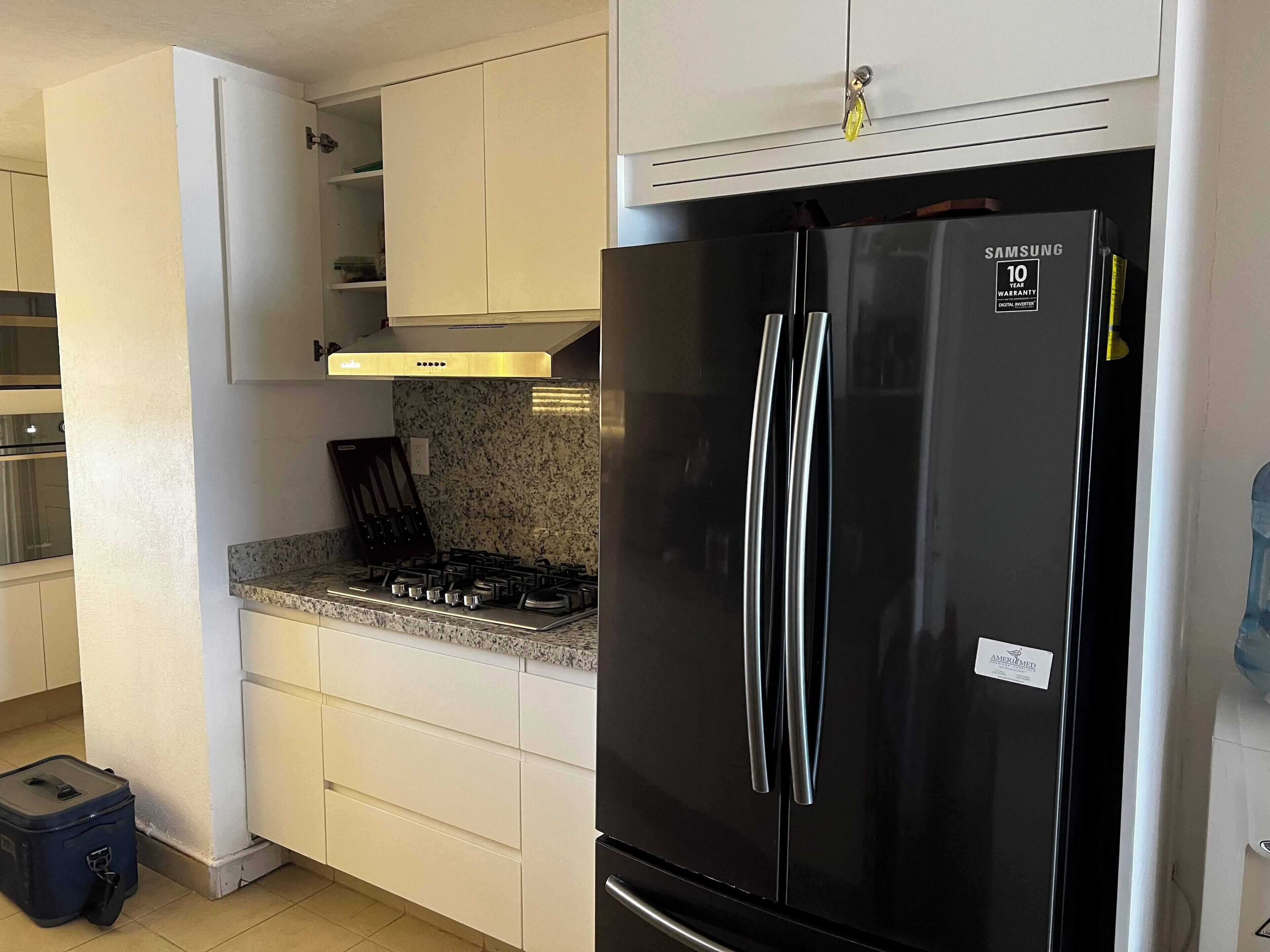 A compact kitchen with white cabinetry, a black Samsung refrigerator, a gas stove, and a small trash bin.