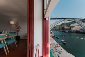 A room with a view of a bridge, a dining area with teal chairs, and a potted plant.