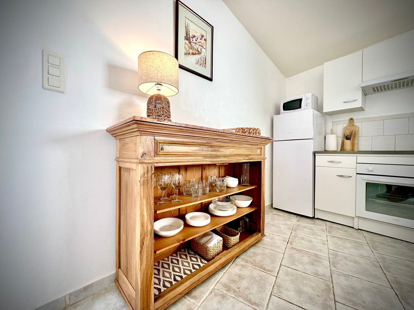 A kitchen with white cabinets, a microwave, and a built-in oven. There is a wooden shelf unit with glassware and bowls.