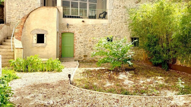 Un edificio de piedra con puerta verde, una ventana pequeña y un balcón con barandillas blancas.