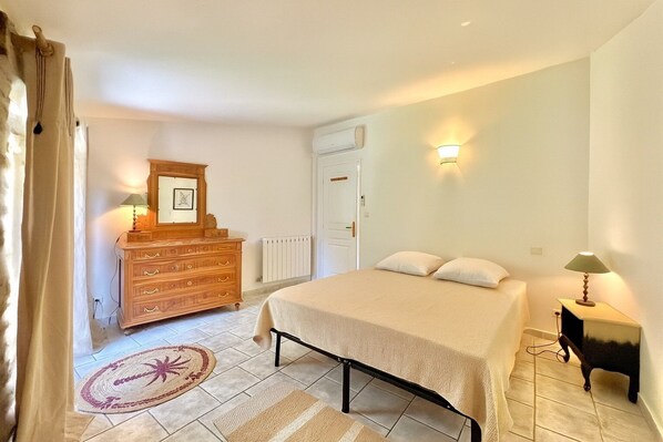 A bedroom with a bed, a dresser, a radiator, a door, and a nightstand with a lamp.