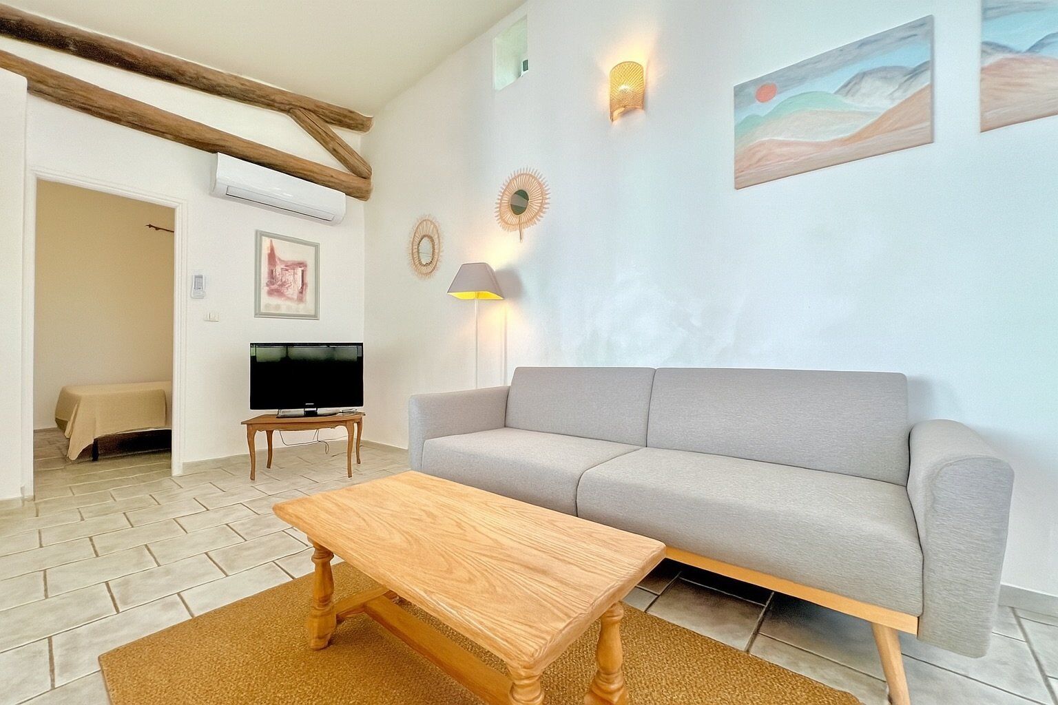 A living room with a grey sofa, a wooden coffee table, a TV on a stand, and a lamp.