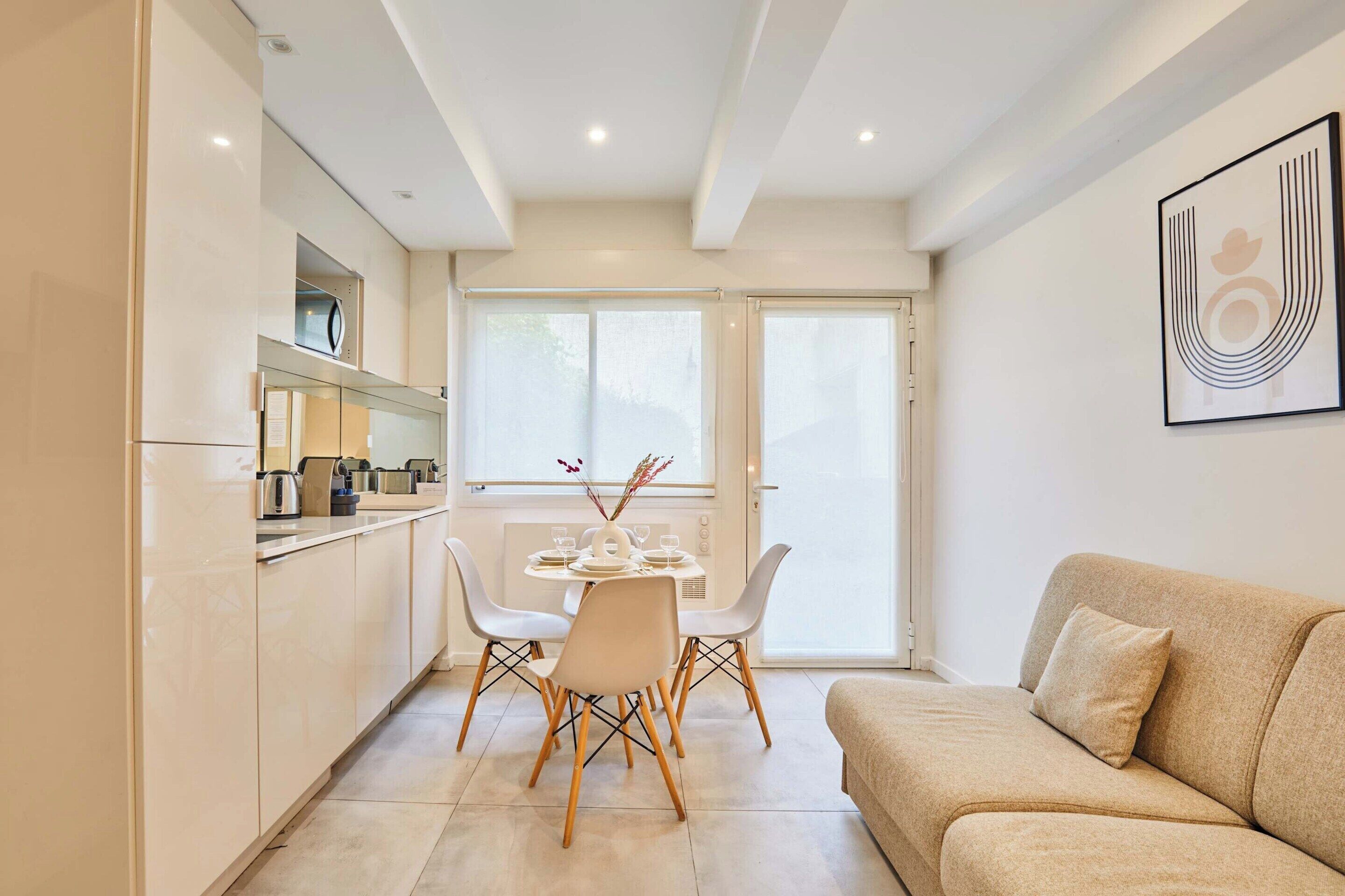 A modern kitchen with a dining table and chairs, a sofa, and a large window.
