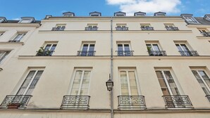 A multi-story building with a symmetrical facade, featuring evenly spaced windows and decorative iron railings on the balconies. - Charming Apartment Center of Paris Le Marais (Paris)