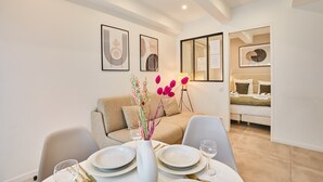 A modern, well-lit room with a dining table set for two, a sofa, and a bed in the background. - Charming Apartment Center of Paris Le Marais (Paris)
