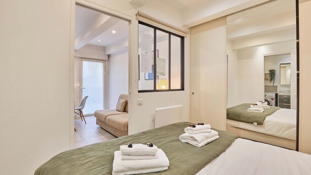 A modern hotel room with a large bed, a sitting area with a chair, and a bathroom with a mirror. - Charming Apartment Center of Paris Le Marais (Paris)