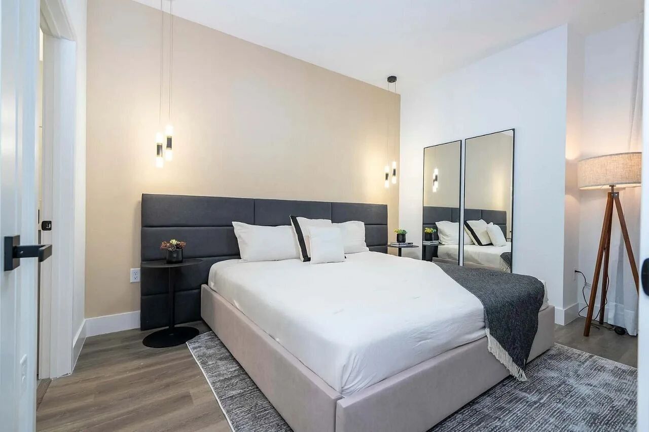 A modern bedroom with a large bed, bedside tables, a mirror, and a lamp.
