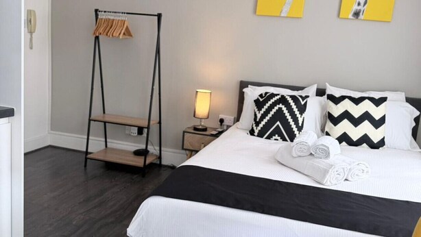 A hotel room with a bed, a nightstand, a lamp, a coat rack, and two wall art pieces.