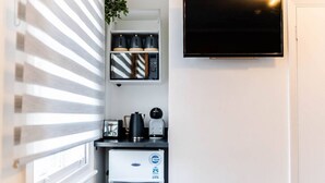 A compact kitchenette with a refrigerator, a coffee maker, a toaster, and a TV mounted on the wall.
