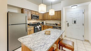 Una cocina con encimeras de granito, gabinetes de madera, electrodomésticos de acero inoxidable e iluminación colgante.