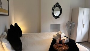 A hotel room with a bed, a mirror, a fan, and a framed picture on the wall.