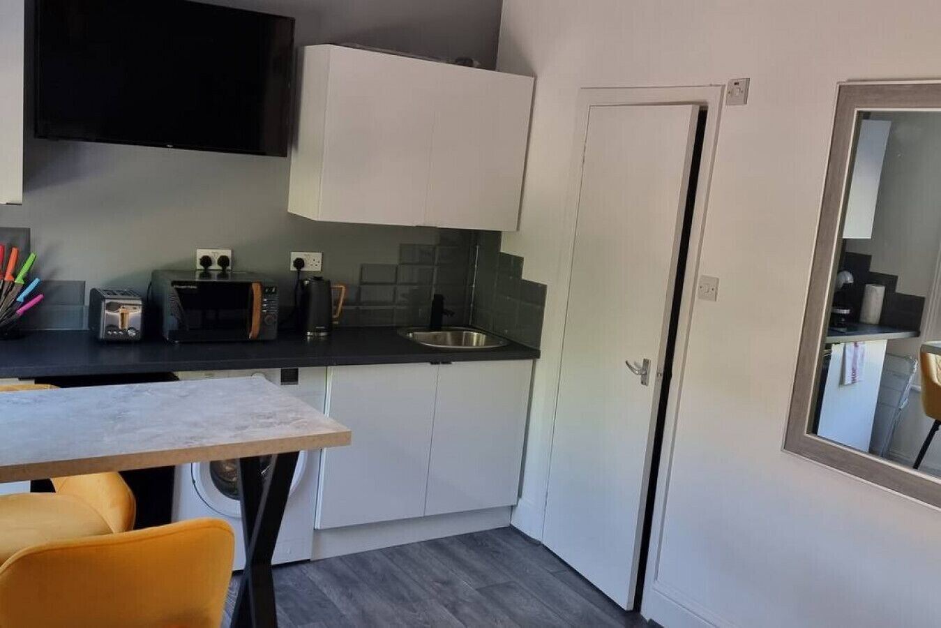 Cozinha compacta com armários brancos, bancada preta, pia e um espaço de refeições com mesa e cadeiras.