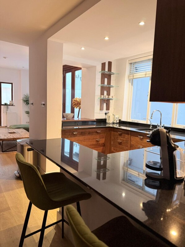 A modern kitchen with a central island, bar stools, and a large window providing natural light.