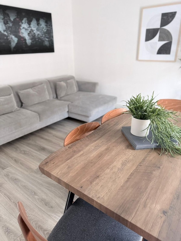 Una sala de estar moderna con una mesa de comedor de madera, un sofá gris y una planta en maceta.