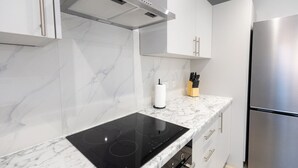 A modern kitchen with white cabinetry, a black induction cooktop, a stainless steel refrigerator, and a marble backsplash.