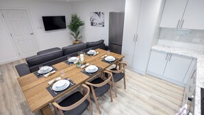 A modern kitchen with white cabinets, a wooden dining table set for four, and a built-in oven. - Market street 33A - 2 - second floor (Watford)