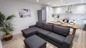 A modern living room with a grey sectional sofa, a wooden dining table set for four, and a kitchen in the background. - Market street 33A - 2 - second floor (Watford)