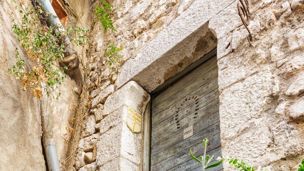 Un bâtiment rustique en pierre, doté d’une porte en bois, de plantes en pot et d’un petit marchepied menant à l’entrée.
