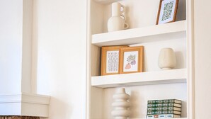 Un mur blanc avec une étagère intégrée où sont posés des livres, un vase et des photos encadrées.
