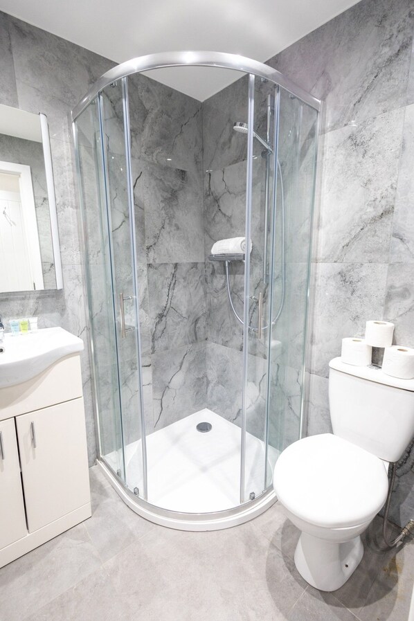 A modern bathroom with a glass-enclosed shower, a white toilet, and a marble-tiled wall.