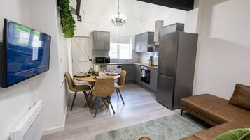 Cozinha moderna com área de refeições, TV de tela plana na parede e sofá na sala de estar.