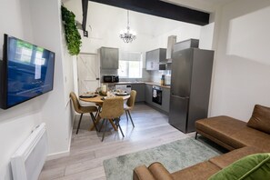 Cozinha moderna com área de refeições, TV de tela plana na parede e sofá na sala de estar.