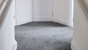 Eine Treppe mit Teppichstufen führt zu einer weißen Tür am Obergeschoss.
