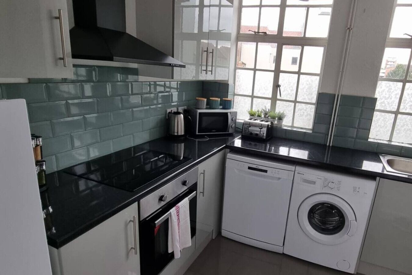 A compact kitchen with a black countertop, a microwave, a toaster, and a washing machine.