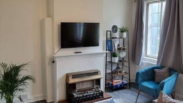 Ein modernes Wohnzimmer mit einem Ecksofa, einem flachbildfernseher an der Wand, einem Kamin und einem fenster mit Vorhängen.