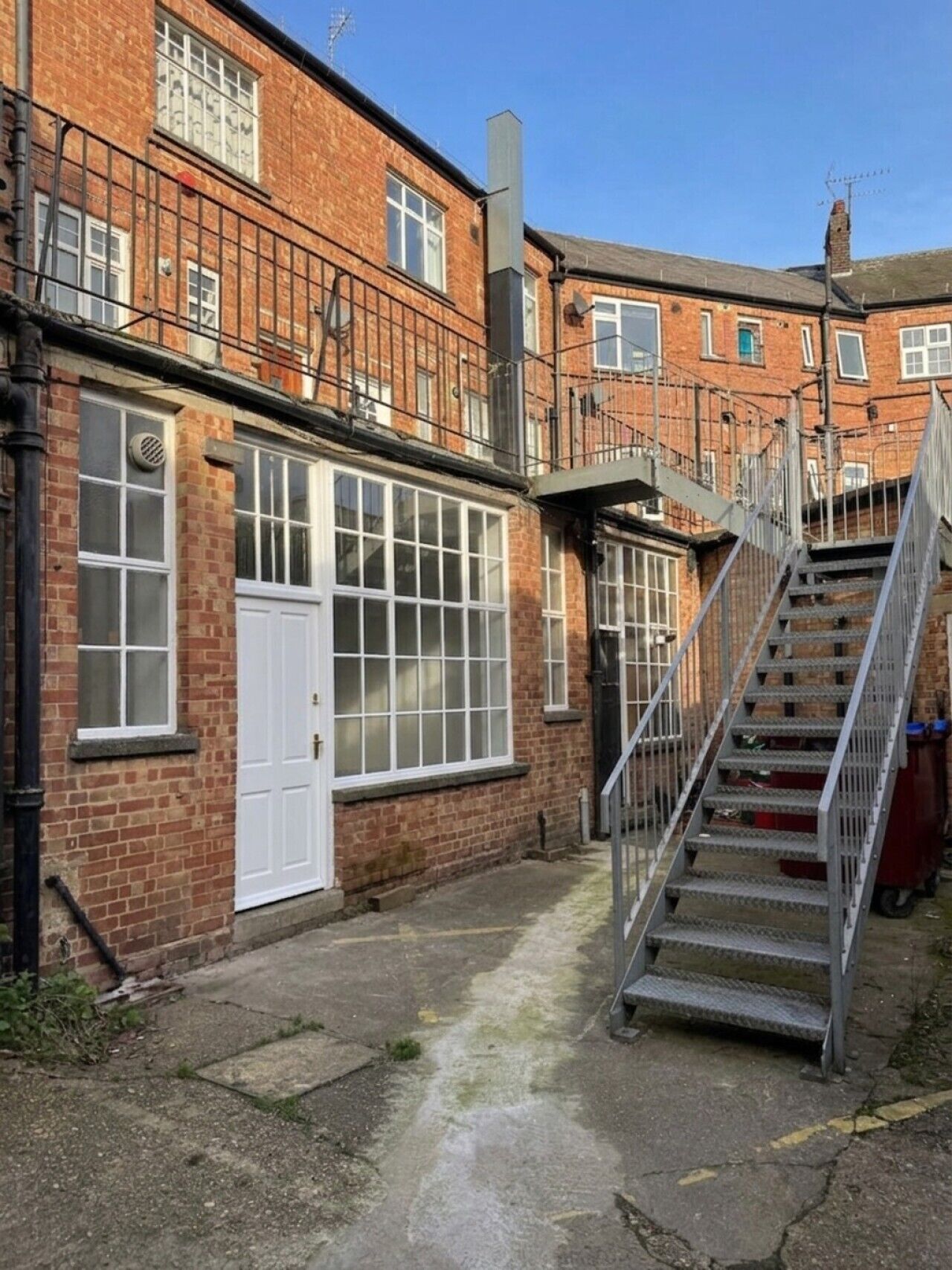 A narrow alleyway with a metal staircase leading to a building with a white door and large windows.