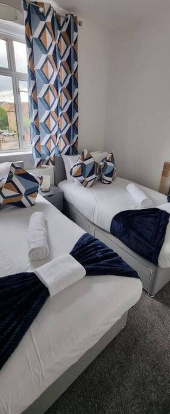 A hotel room with two beds, a window, and a geometric-patterned curtain. - Faircross. (Watford)