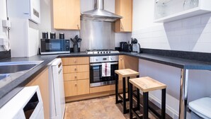 A modern kitchen with a built-in microwave, stove, and oven. There are wooden cabinets, a sink, and two stools.