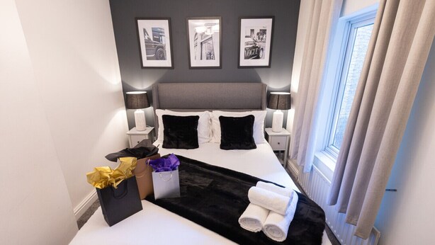 A hotel room with a bed, two bedside tables, a window with curtains, and framed pictures on the wall.