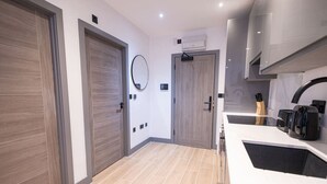 A modern kitchen with a white countertop, a sink, and a coffee machine. There are two wooden doors and a mirror on the wall. - Avenir Court Flat 5 (Finchley) (Greater London)