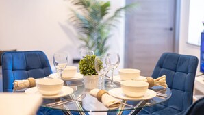 A dining table set with plates, bowls, and wine glasses, surrounded by blue upholstered chairs. - Avenir Court Flat 5 (Finchley) (Greater London)